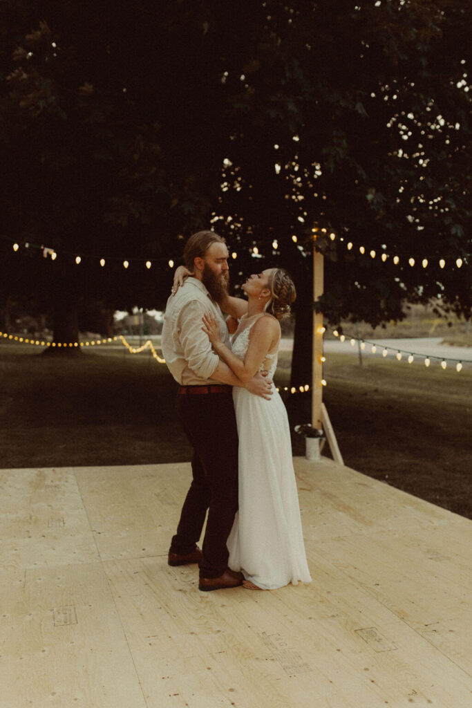 Bride and groom first dance on outdoor platform with string lights
