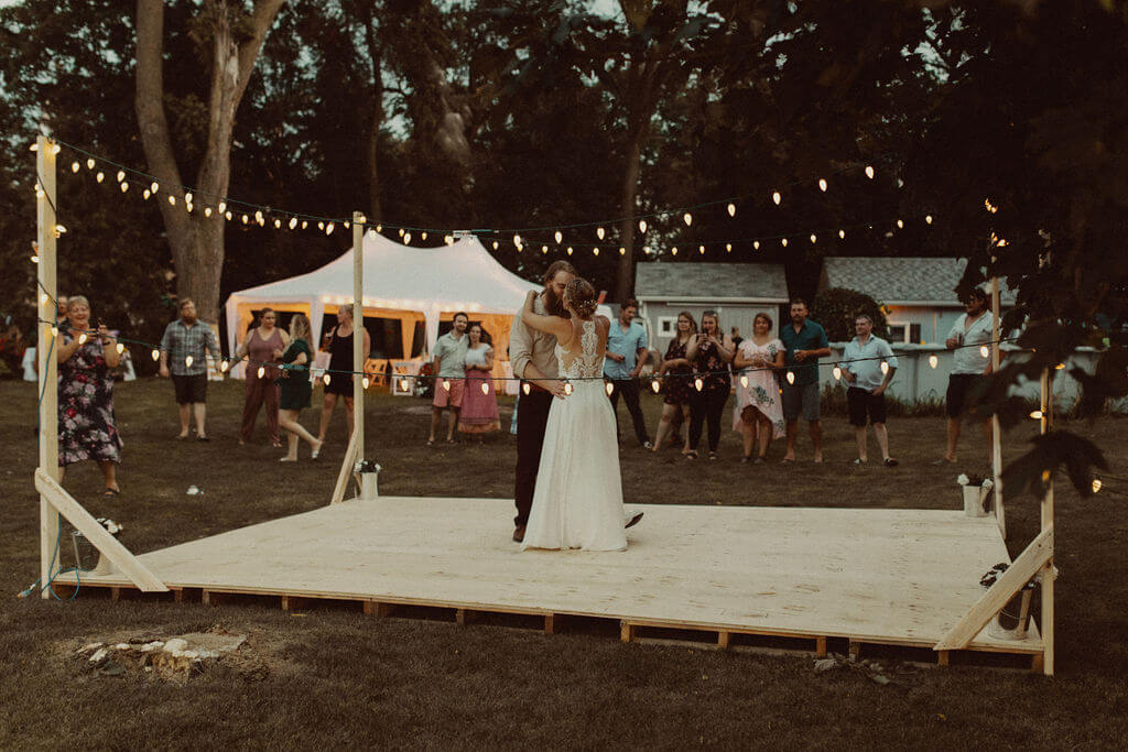 Bride and groom first dance on outdoor platform with string lights