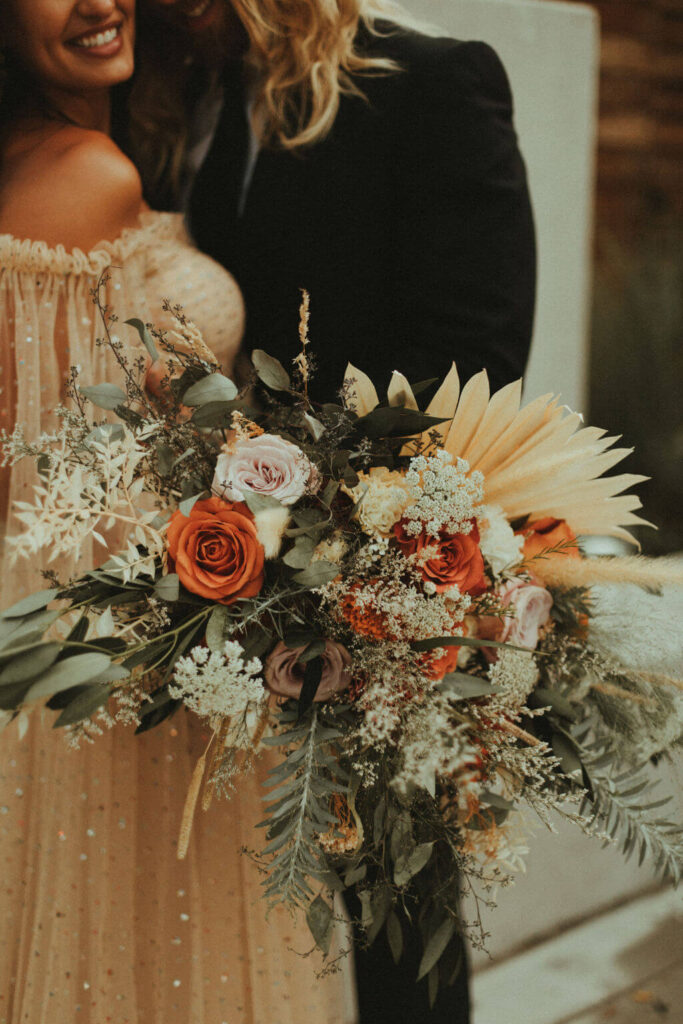 Bride holding orange, white and pink floral bouquet