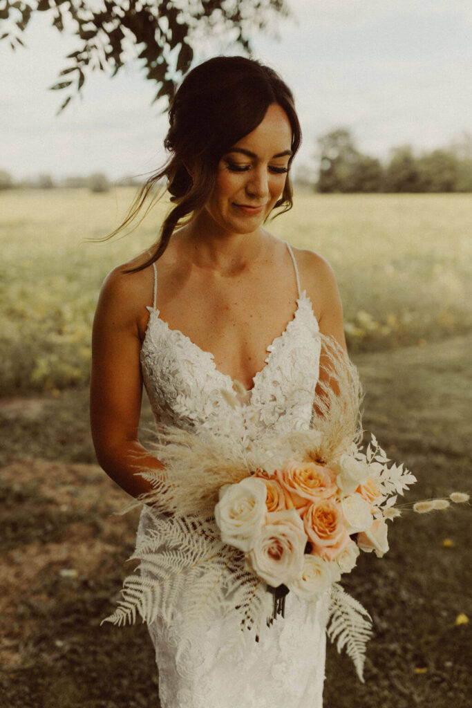 Bride wearing lace wedding dress and holding white and peach floral bouquet