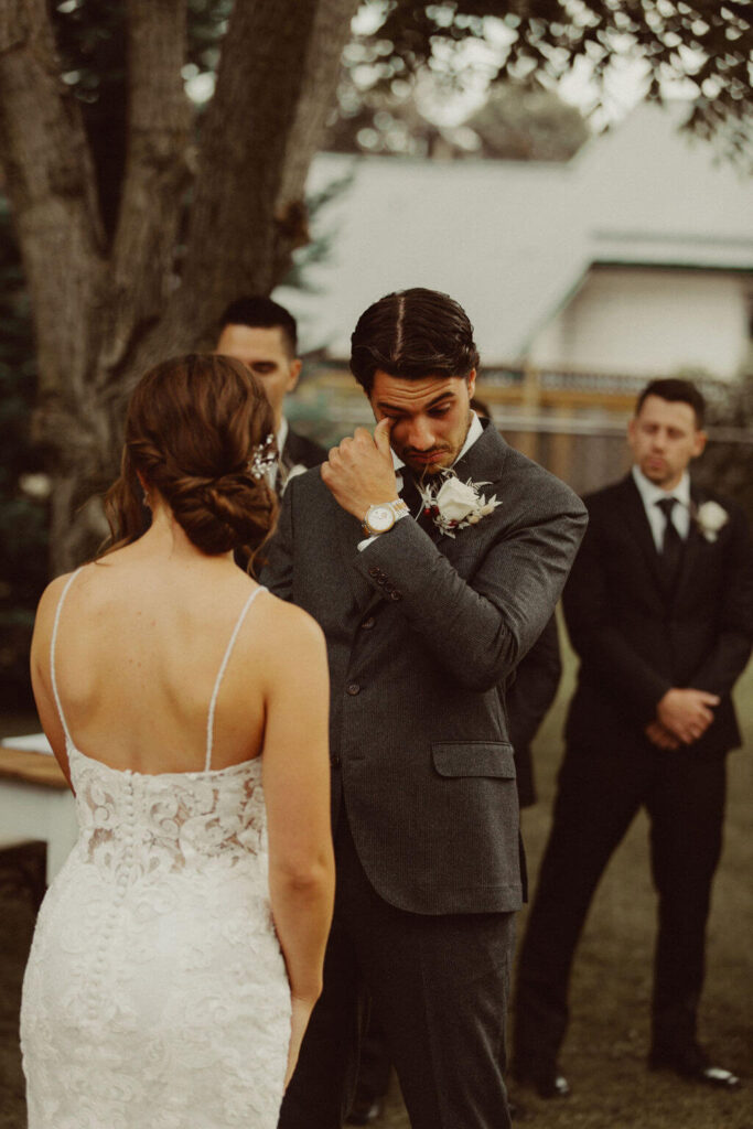 Groom wiping tears during backyard wedding ceremony