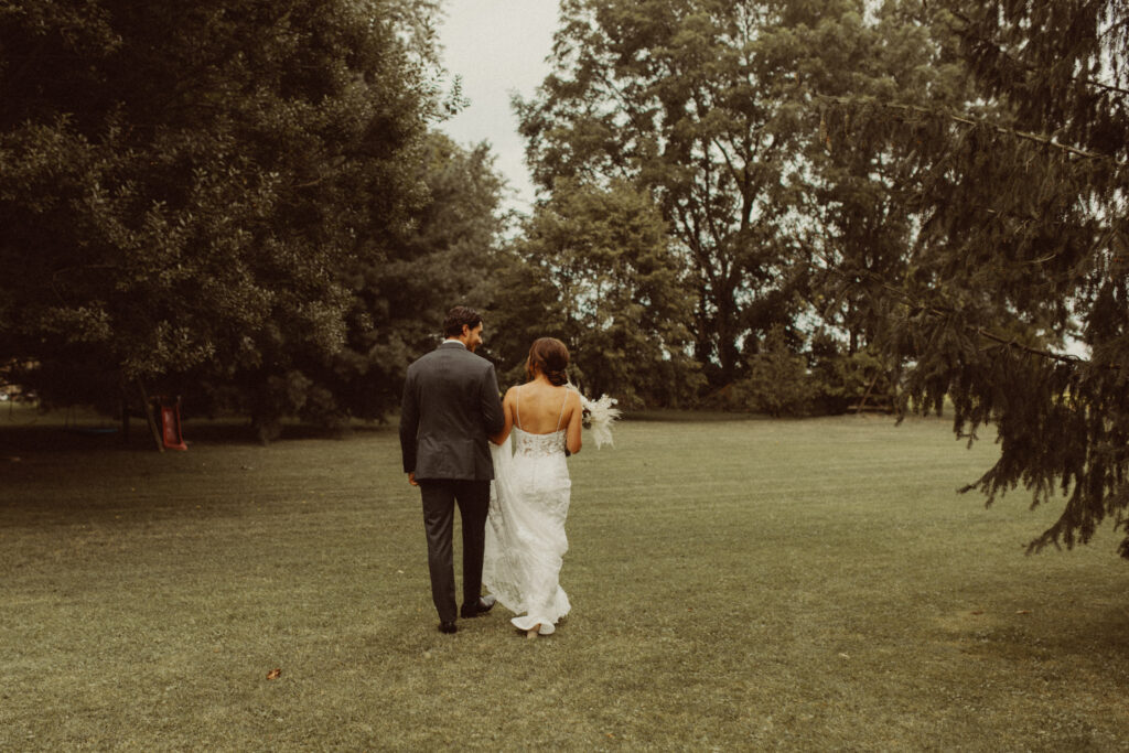A couple walking on a field of grass together during their intimate backyard wedding.