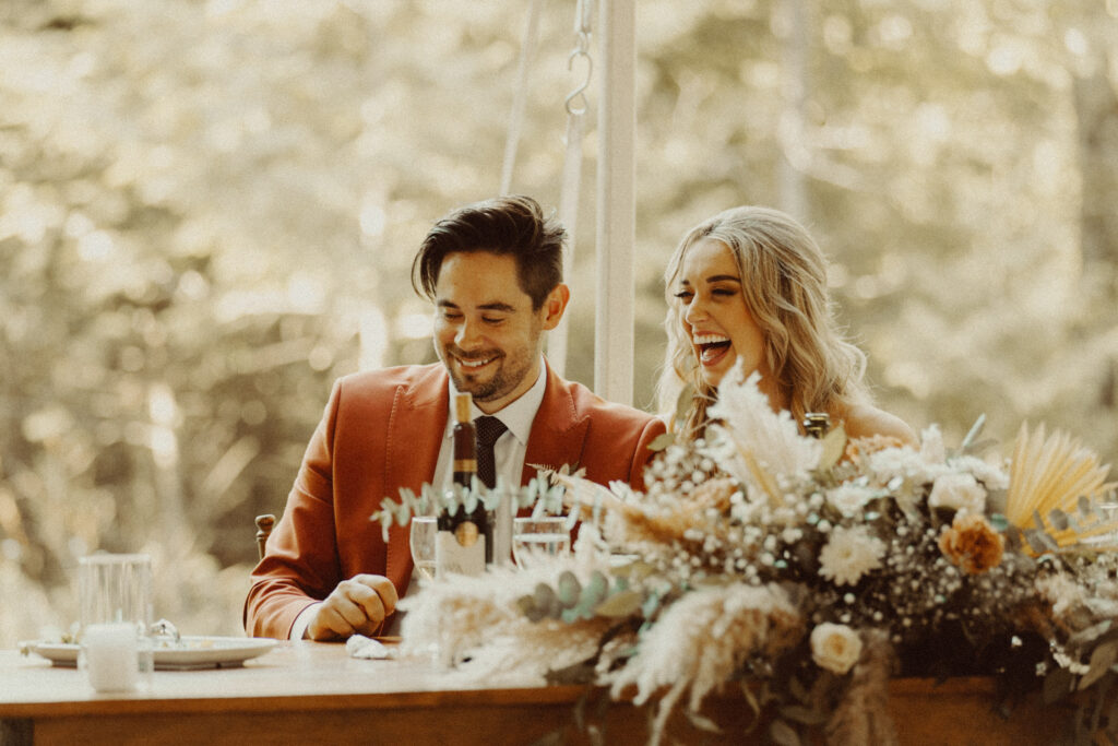 A couple sitting together at the table, laughing during their intimate backyard wedding.