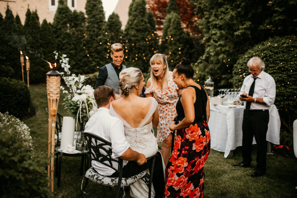 A couple laughing and chatting with their guests during the reception for their intimate backyard wedding.