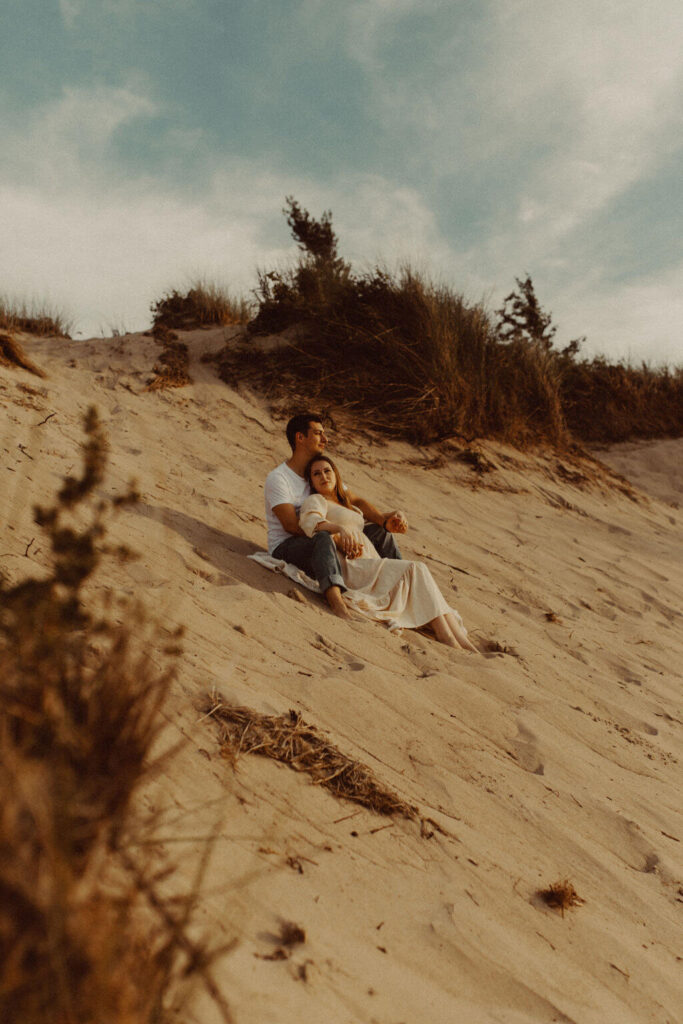 Couple sitting on the sand dunes during engagement session