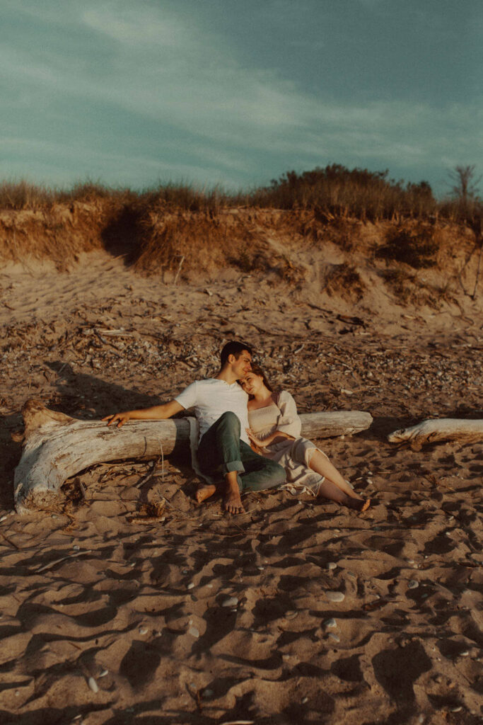 Couple sitting on the beach during Lake Huron engagement session