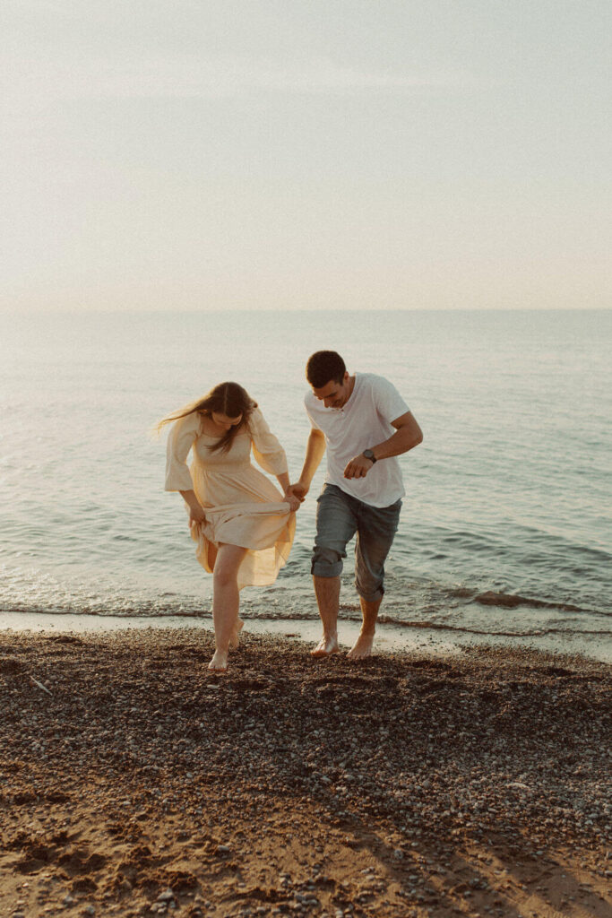 Couple holding hands running along the beach at Lake Huron