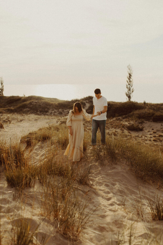Couple holding hands and walking during Lake Huron sand dune engagement session
