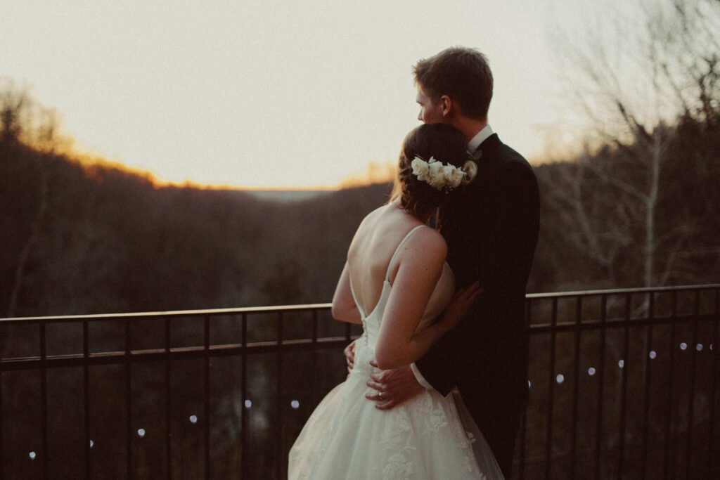 A couple is standing on a balcony, watching the sunset on their elopement day.