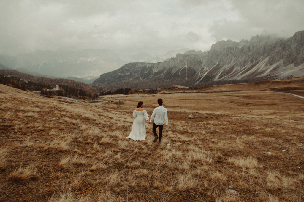 A couple walking in a field during their destination wedding in the Dolomites.